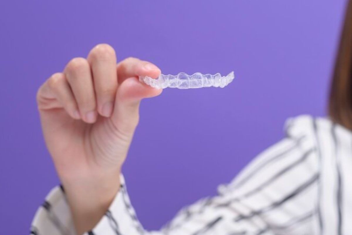 person holding a clear invisalign aligner, illustrating the treatment timeline for teeth straightening.
